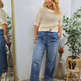 Woman wearing cream knit sweater and blue drawstring denim pants with woven sandals, styled casually in boho-inspired setting