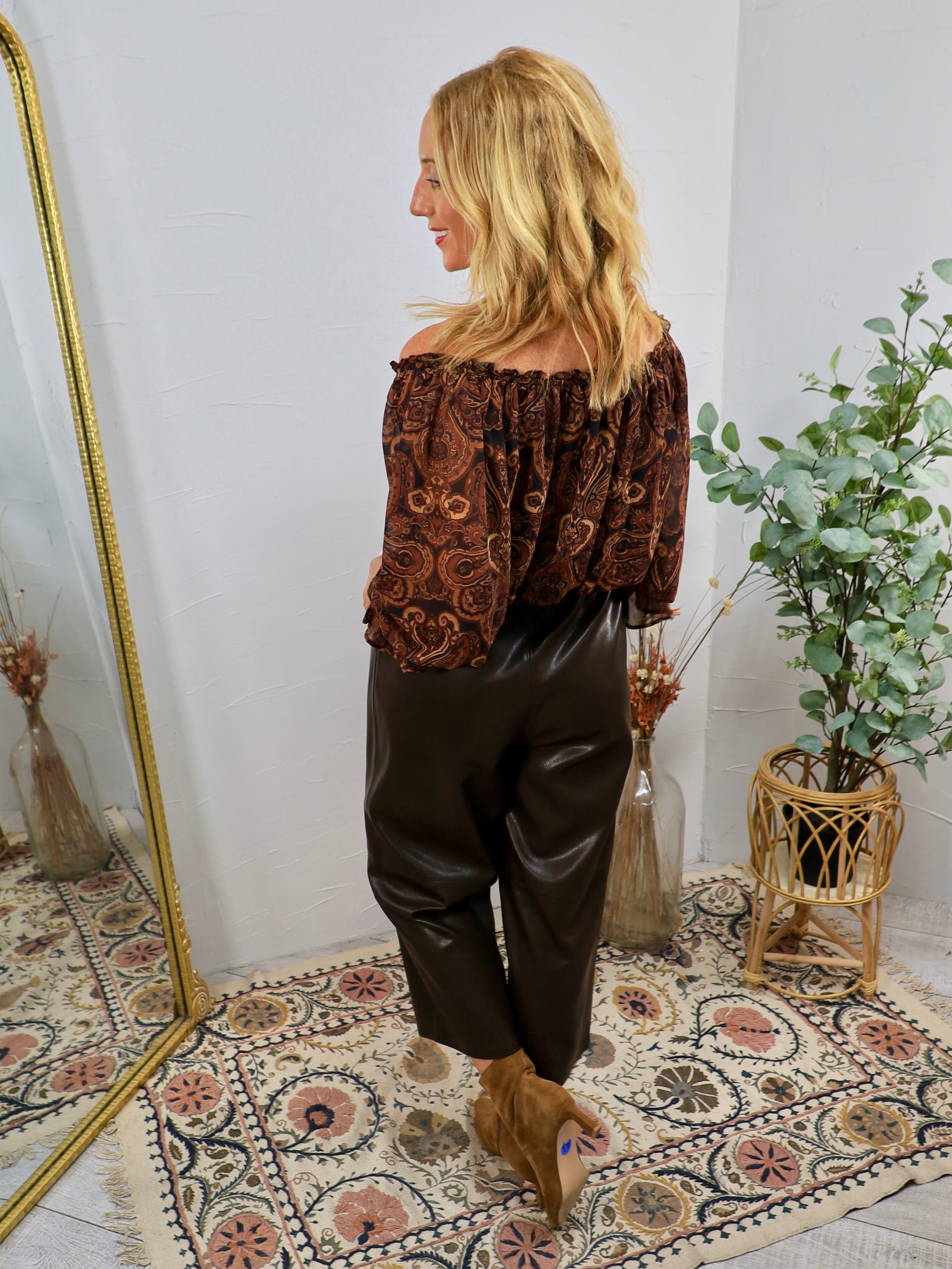 Dark brown faux leather cropped pants styled with paisley off-shoulder top and tan booties.