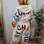 Cream joggers with colorful chenille "Merry Christmas" lettering, paired with matching hoodie, modeled from behind.
