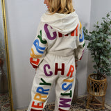 Cream joggers with colorful chenille "Merry Christmas" lettering, paired with matching hoodie, modeled from behind.