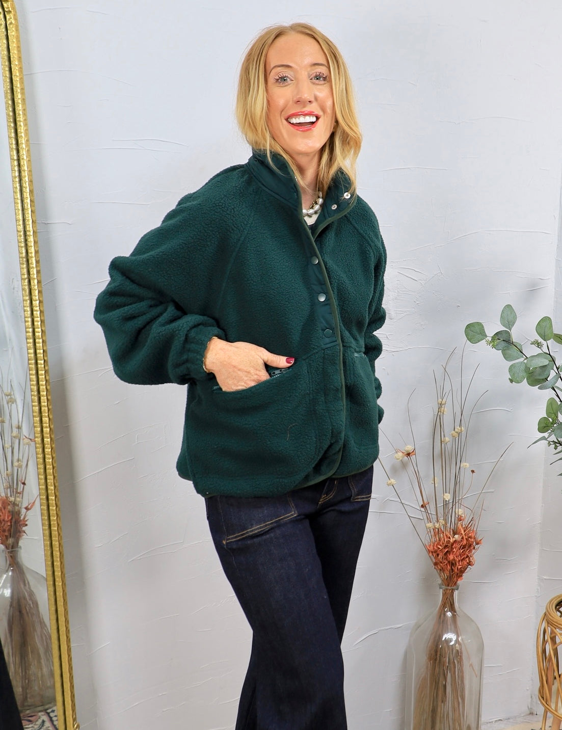 Forest green sherpa pullover with snap buttons, worn over dark jeans, featuring front pockets and a mock neck.