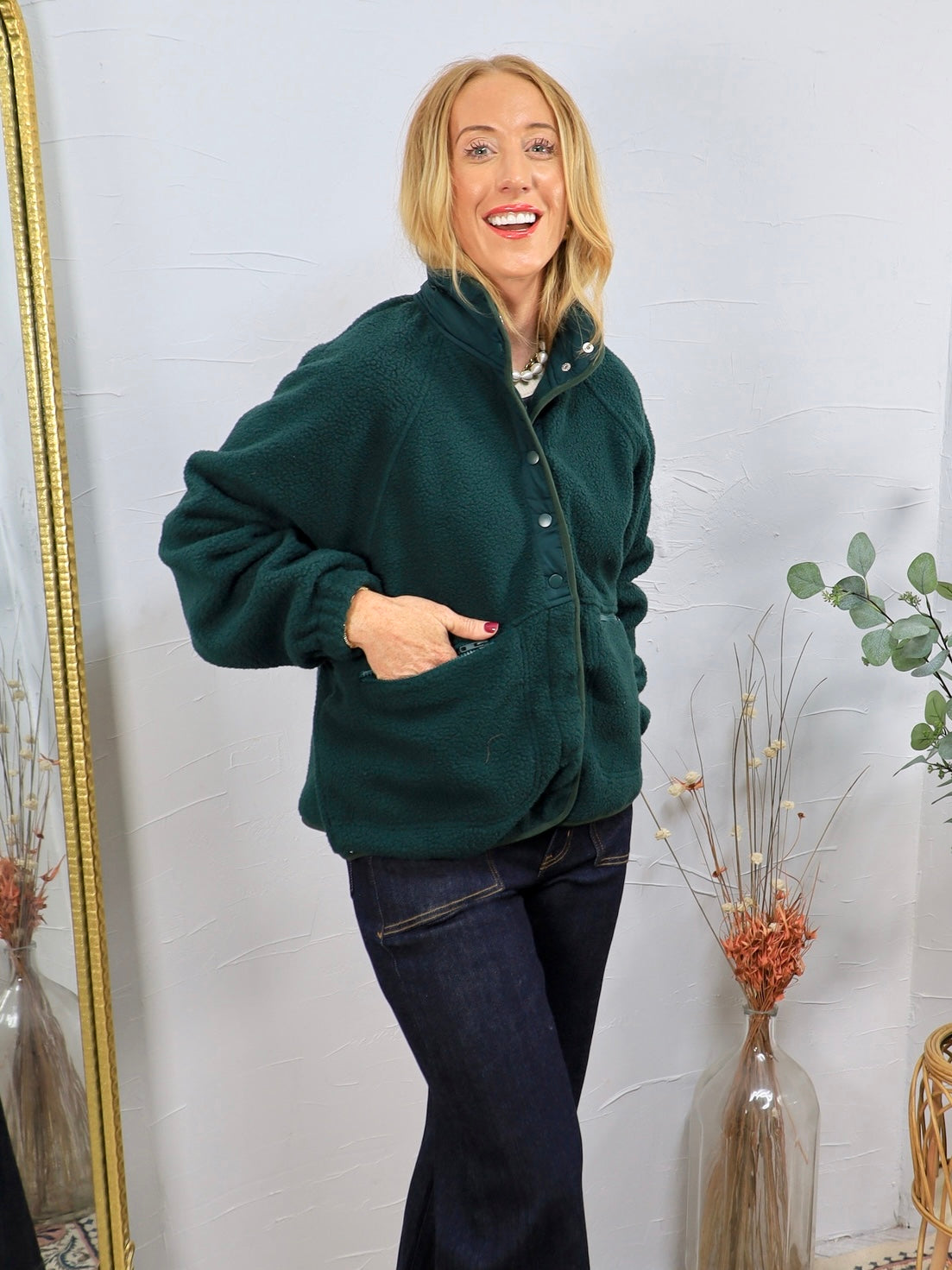Forest green sherpa pullover with snap buttons, worn over dark jeans, featuring front pockets and a mock neck.