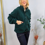 Forest green sherpa pullover with snap buttons, worn over dark jeans, featuring front pockets and a mock neck.