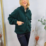 Forest green sherpa pullover with snap buttons, worn over dark jeans, featuring front pockets and a mock neck.