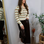 Woman wearing a cream striped sage and brown cropped button-up cardigan with a dark midi skirt and brown booties