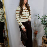 Woman wearing a cream striped sage and brown cropped button-up cardigan with a dark midi skirt and brown booties