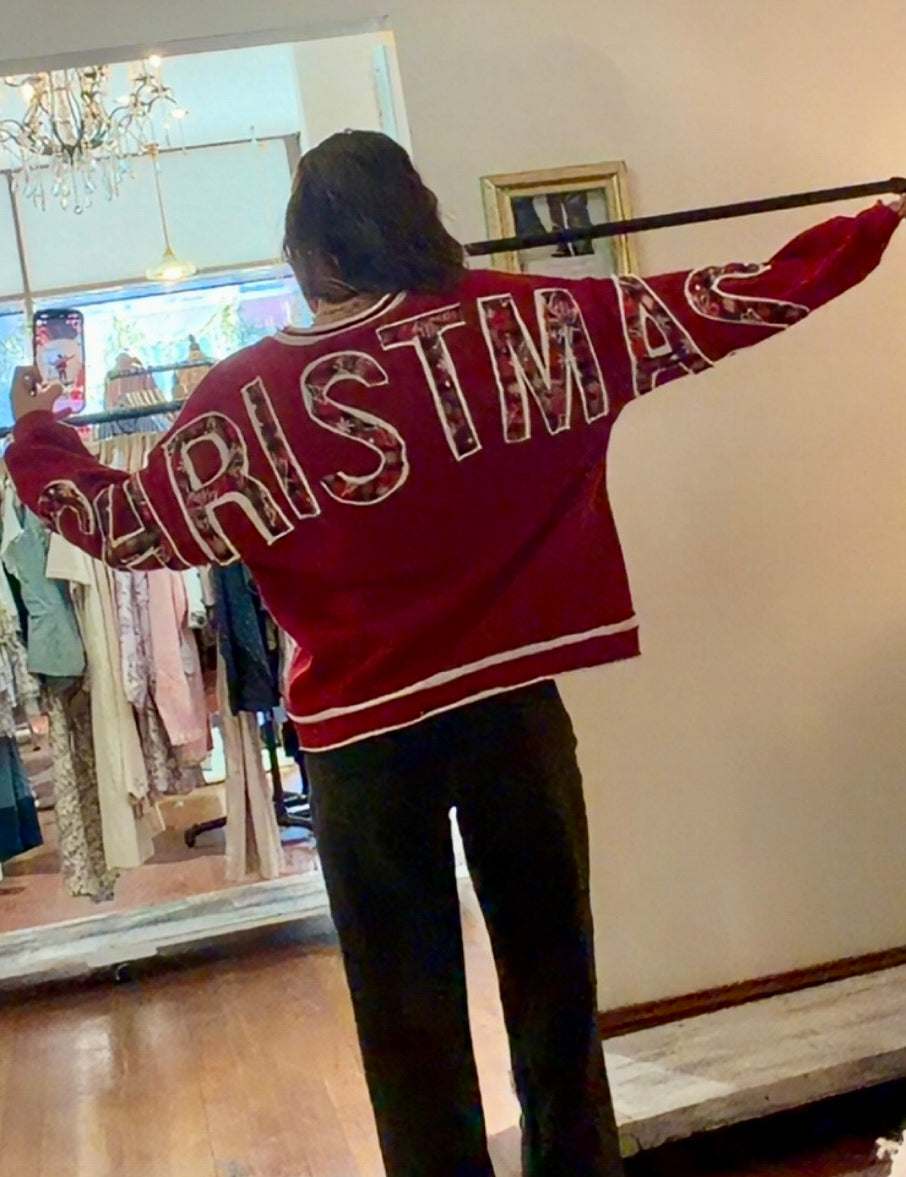 Model wearing red Christmas crewneck sweatshirt with bold festive letter appliqués across the back