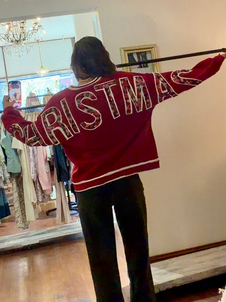 Model wearing red Christmas crewneck sweatshirt with bold festive letter appliqués across the back