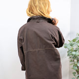 Back view of an oversized dark brown utility jacket with contrast stitching, worn with blue jeans.