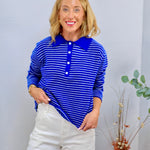 Woman wearing a royal blue and white striped long-sleeve polo sweater top with button placket, paired with white wide-leg pan