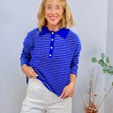 Woman wearing a royal blue and white striped long-sleeve polo sweater top with button placket, paired with white wide-leg pan