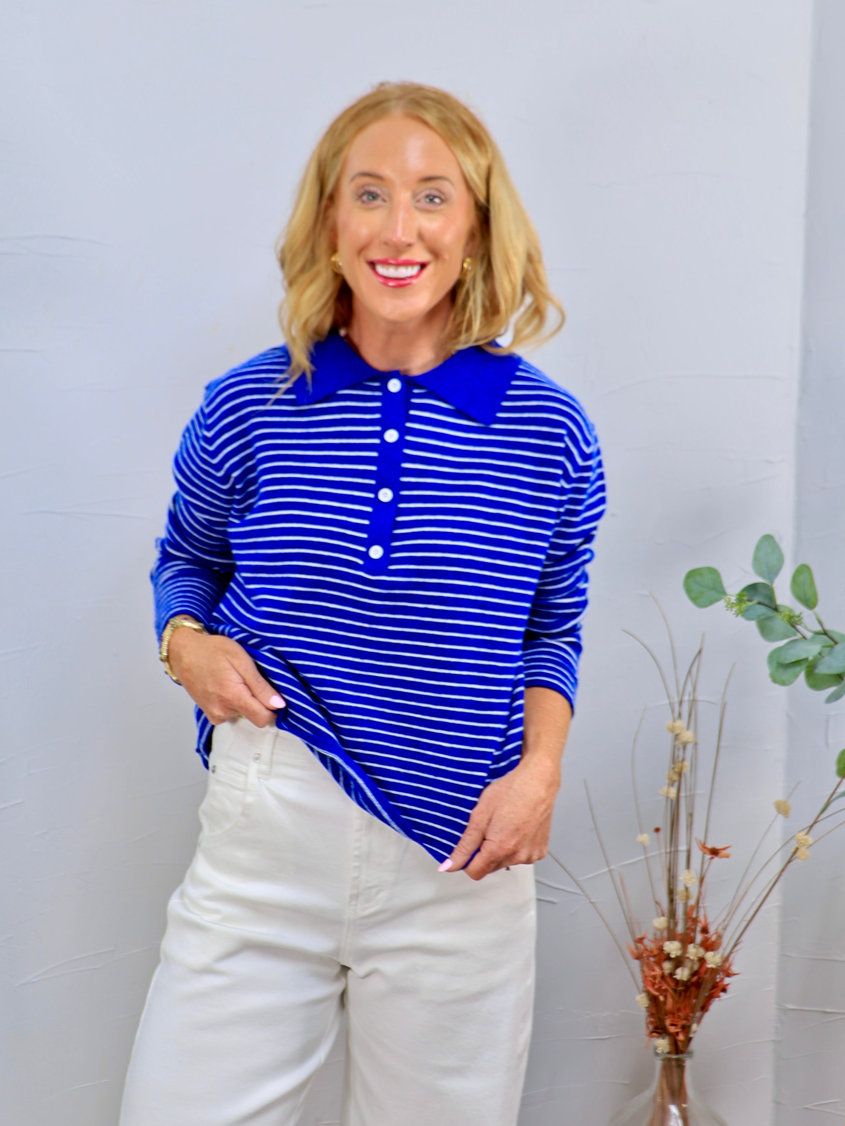 Woman wearing a royal blue and white striped long-sleeve polo sweater top with button placket, paired with white wide-leg pan