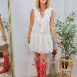 Woman wearing a white ruffle V-neck mini dress with bold red cowboy boots, smiling joyfully