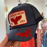 Navy blue suede trucker hat with red embroidered "The American Dream USA 1776" eagle patch and feather brim detail.