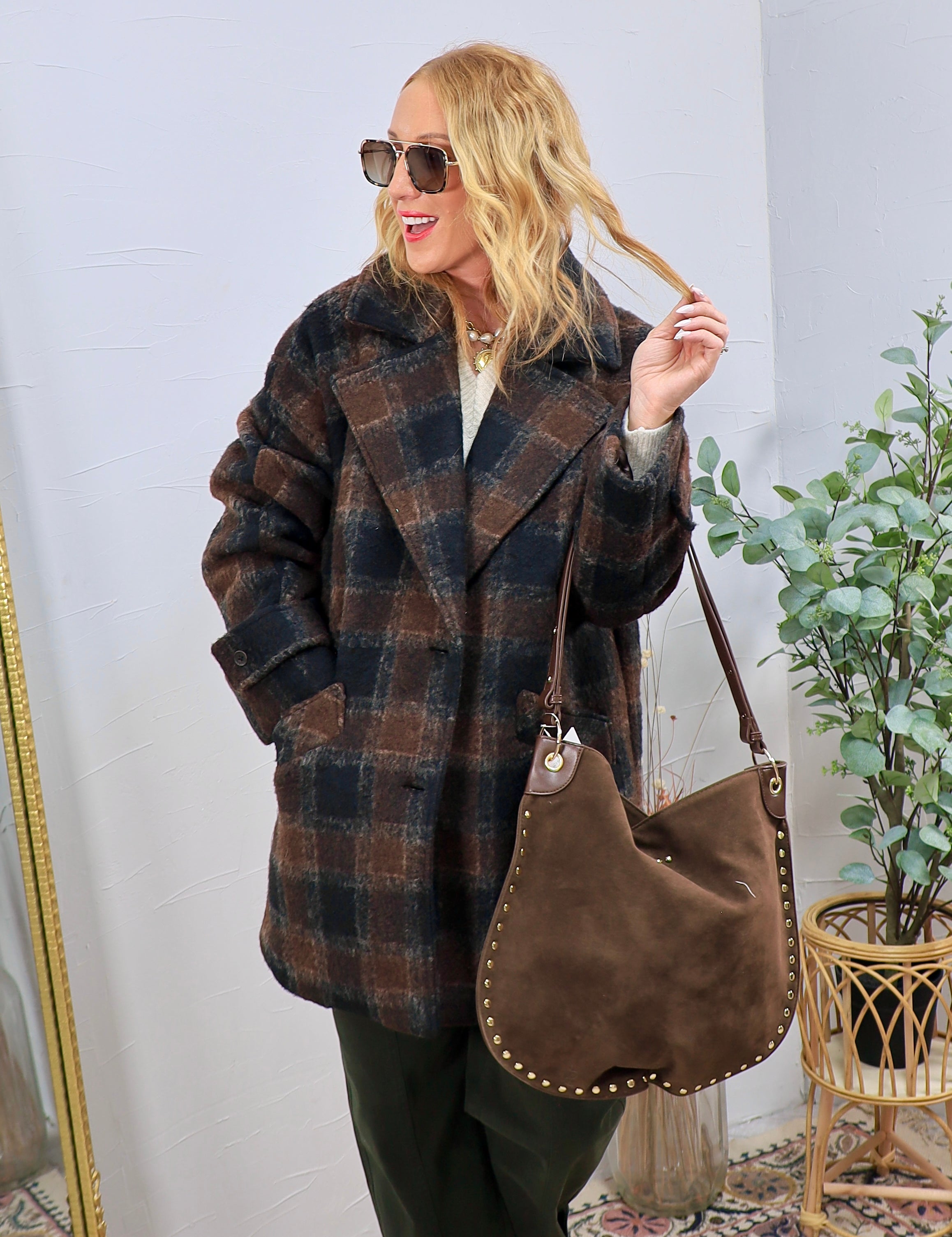 Woman wearing oversized brown and navy plaid wool jacket with suede studded hobo bag