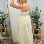 Woman in cream strapless maxi dress with smocked waist detail, styled with beaded earrings in bohemian room setting.