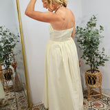 Woman in cream strapless maxi dress with smocked waist detail, styled with beaded earrings in bohemian room setting.