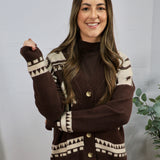 Brown and cream geometric patterned cardigan with gold buttons, layered over dark turtleneck, modeled by smiling woman.