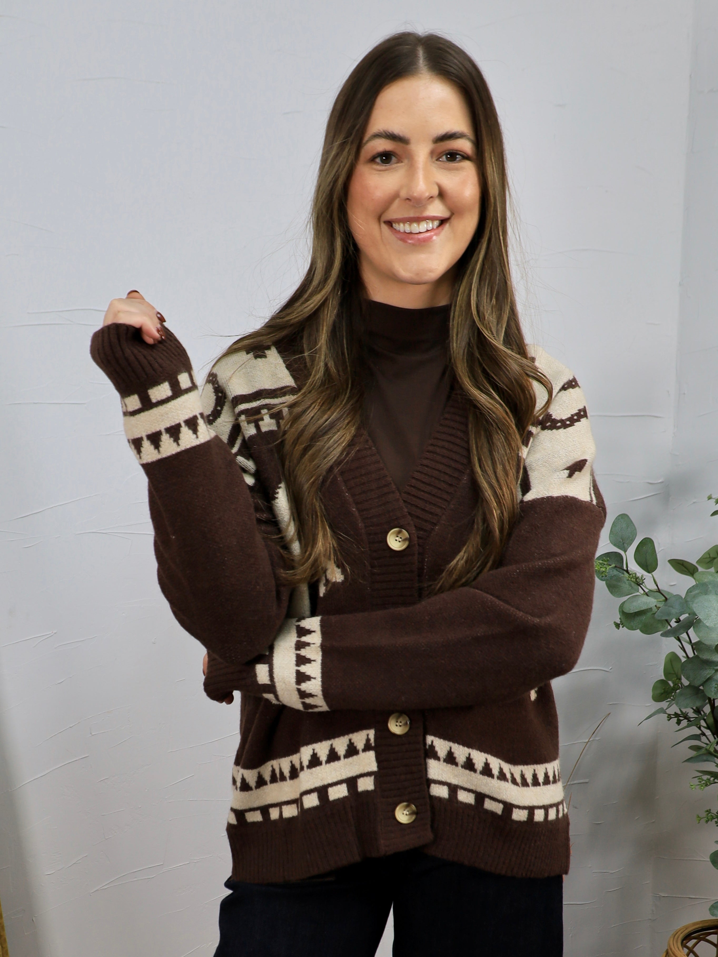 Brown and cream geometric patterned cardigan with gold buttons, layered over dark turtleneck, modeled by smiling woman.