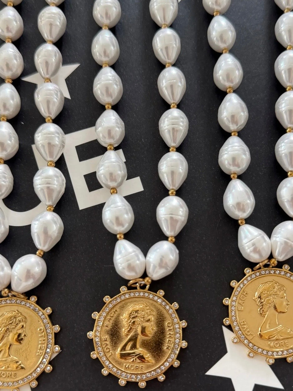 Pearl beaded necklace with gold coin pendant engraved "Love Each Other More," adorned with crystal halo border.