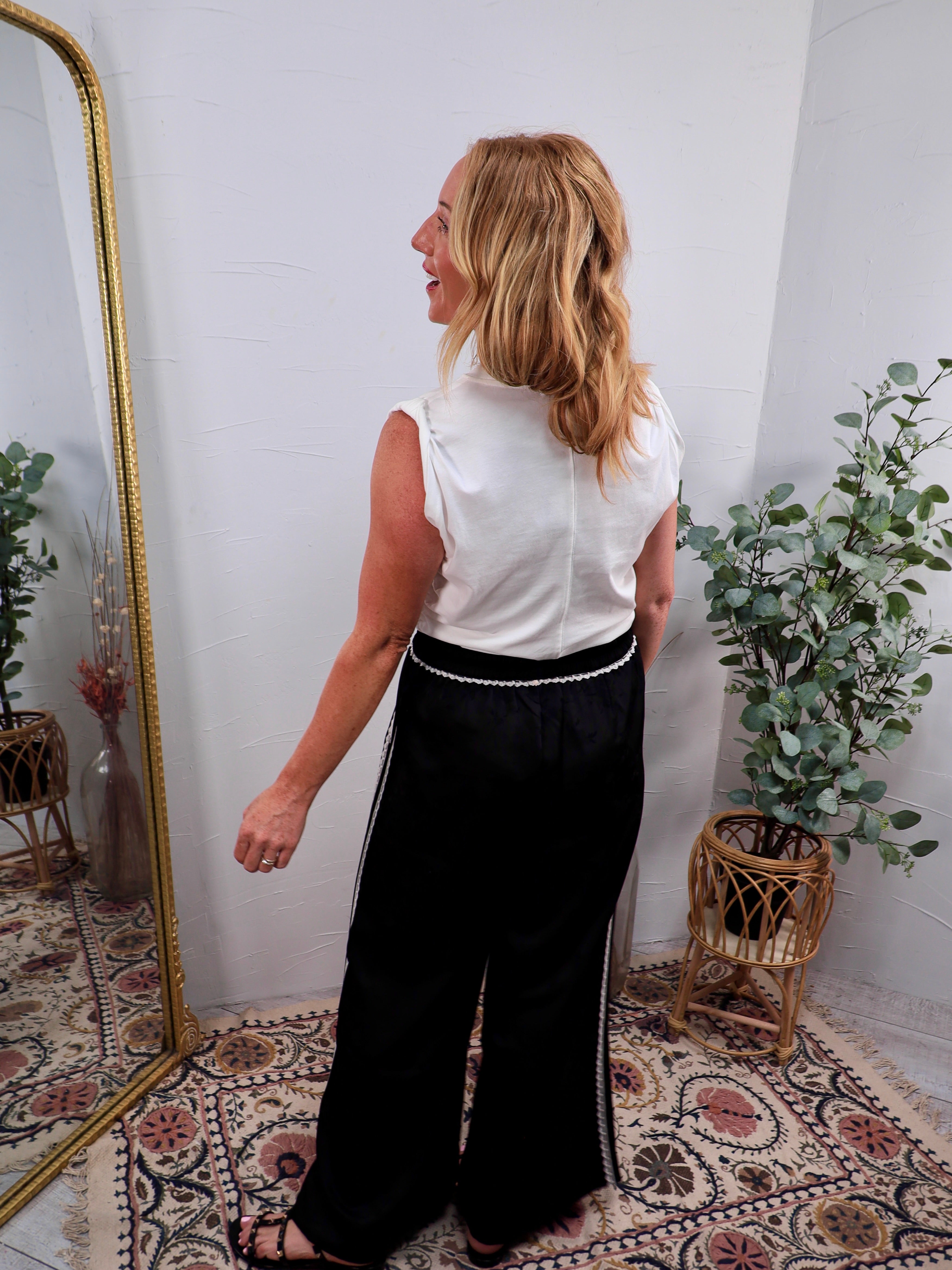 White sleeveless Luna Top tucked into wide-leg black trousers with white trim detailing.