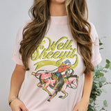 Woman wearing light pink graphic tee with vintage cowboy design and Well Sheeyit text