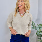Beige v-neck knit sweater styled with dark blue jeans, gold coin necklace, and pearl chain layered necklace.
