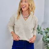 Beige v-neck knit sweater styled with dark blue jeans, gold coin necklace, and pearl chain layered necklace.