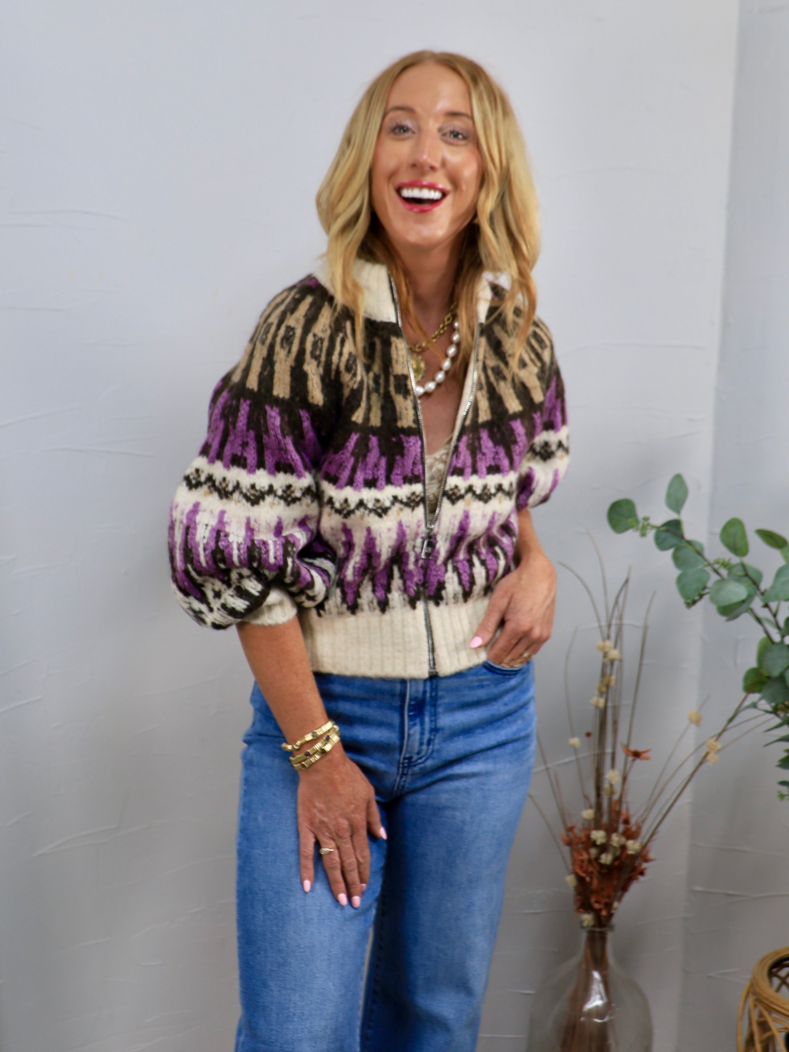 Cream, purple, and black Fair Isle zip-up sweater with puff sleeves, styled with blue jeans and gold jewelry.