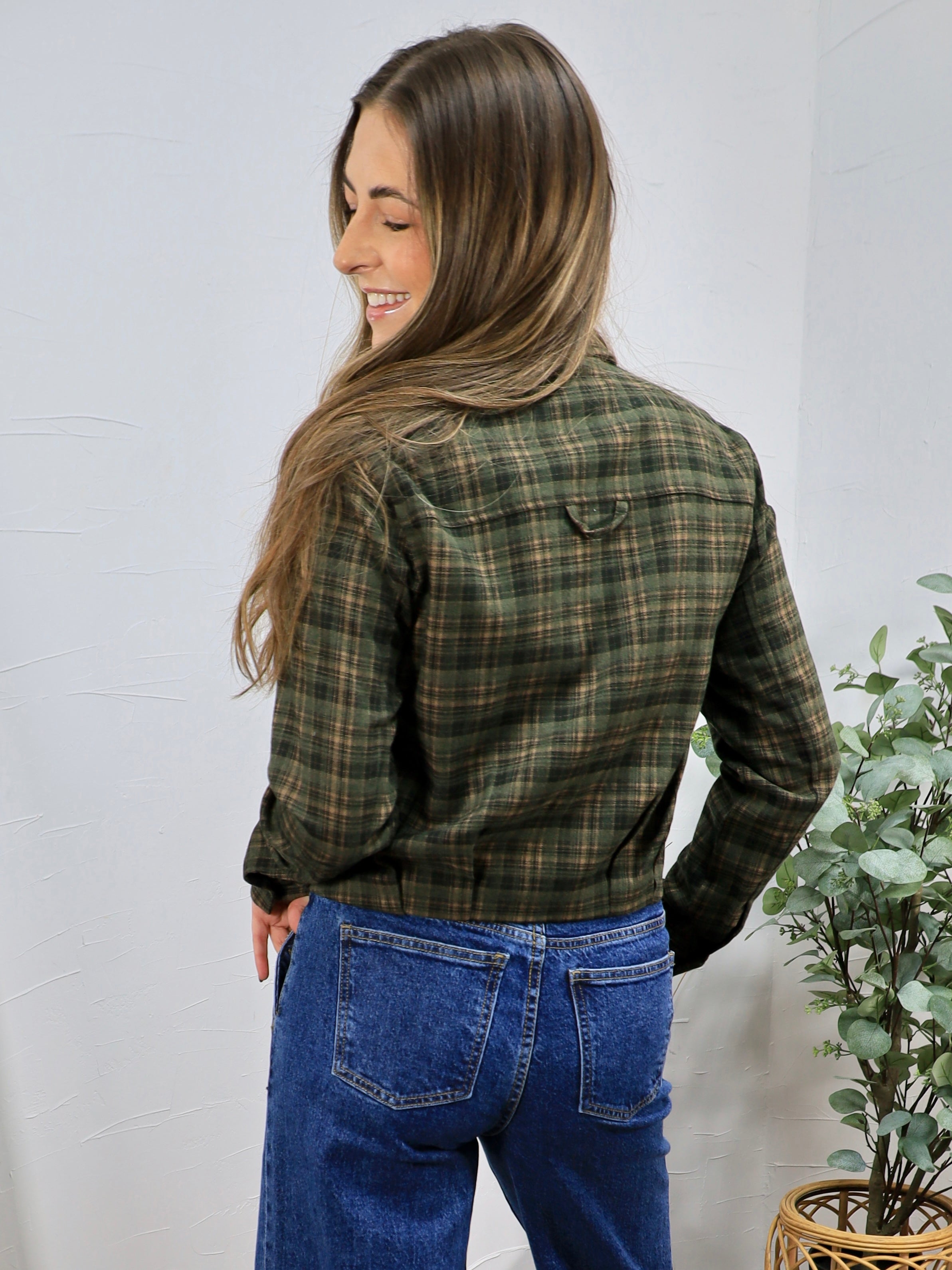 Olive green plaid flannel button-up shirt styled with blue wide-leg jeans, shown from back view.