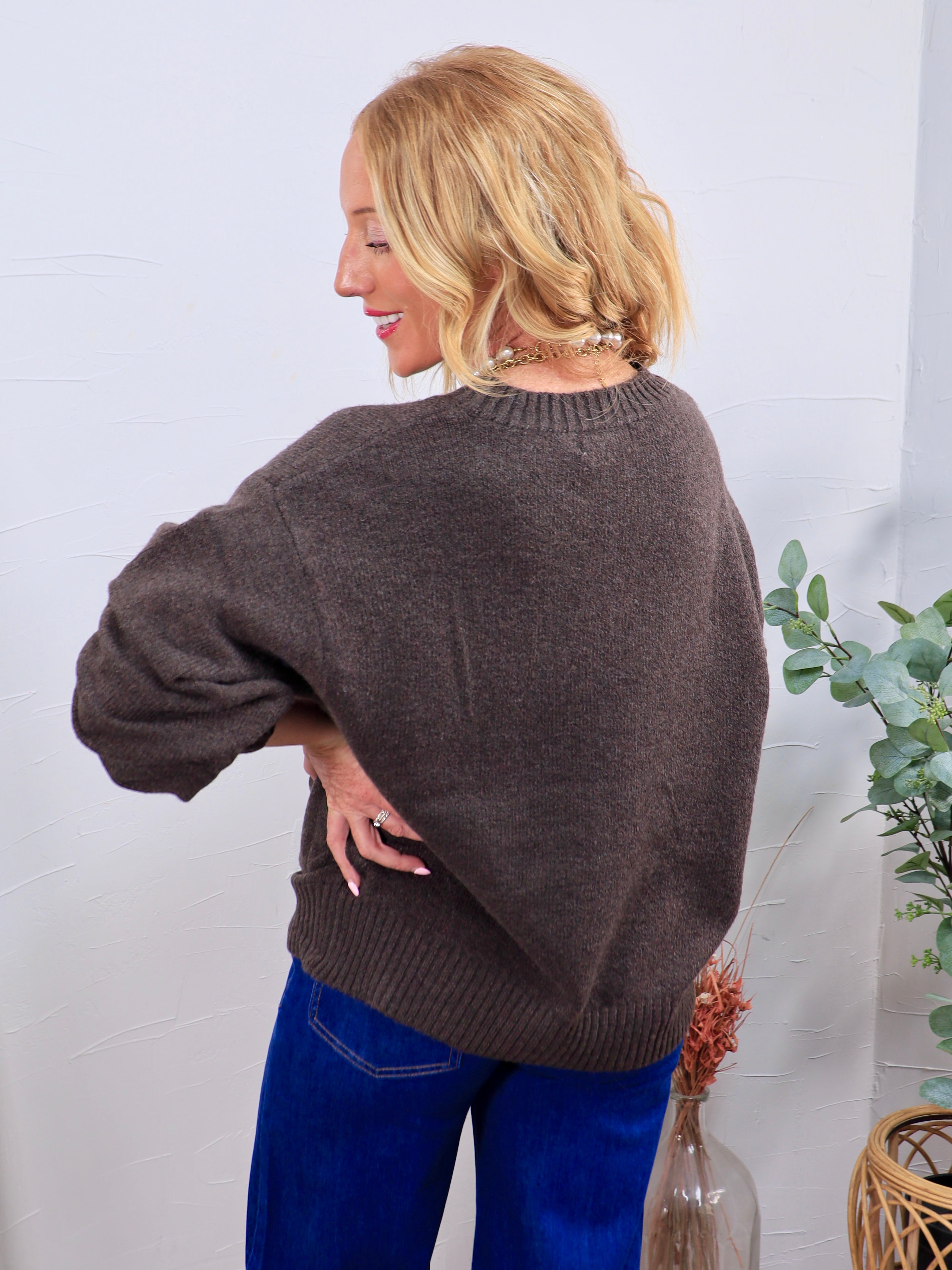 Charcoal brown crewneck sweater with ribbed hem, shown from back, styled with blue wide-leg jeans.