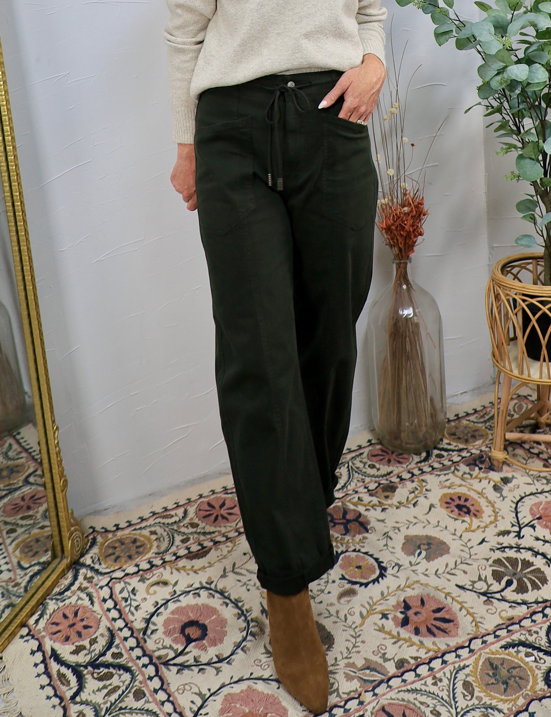 Woman wearing dark fern green drawstring tapered pants with cream sweater and tan ankle boots