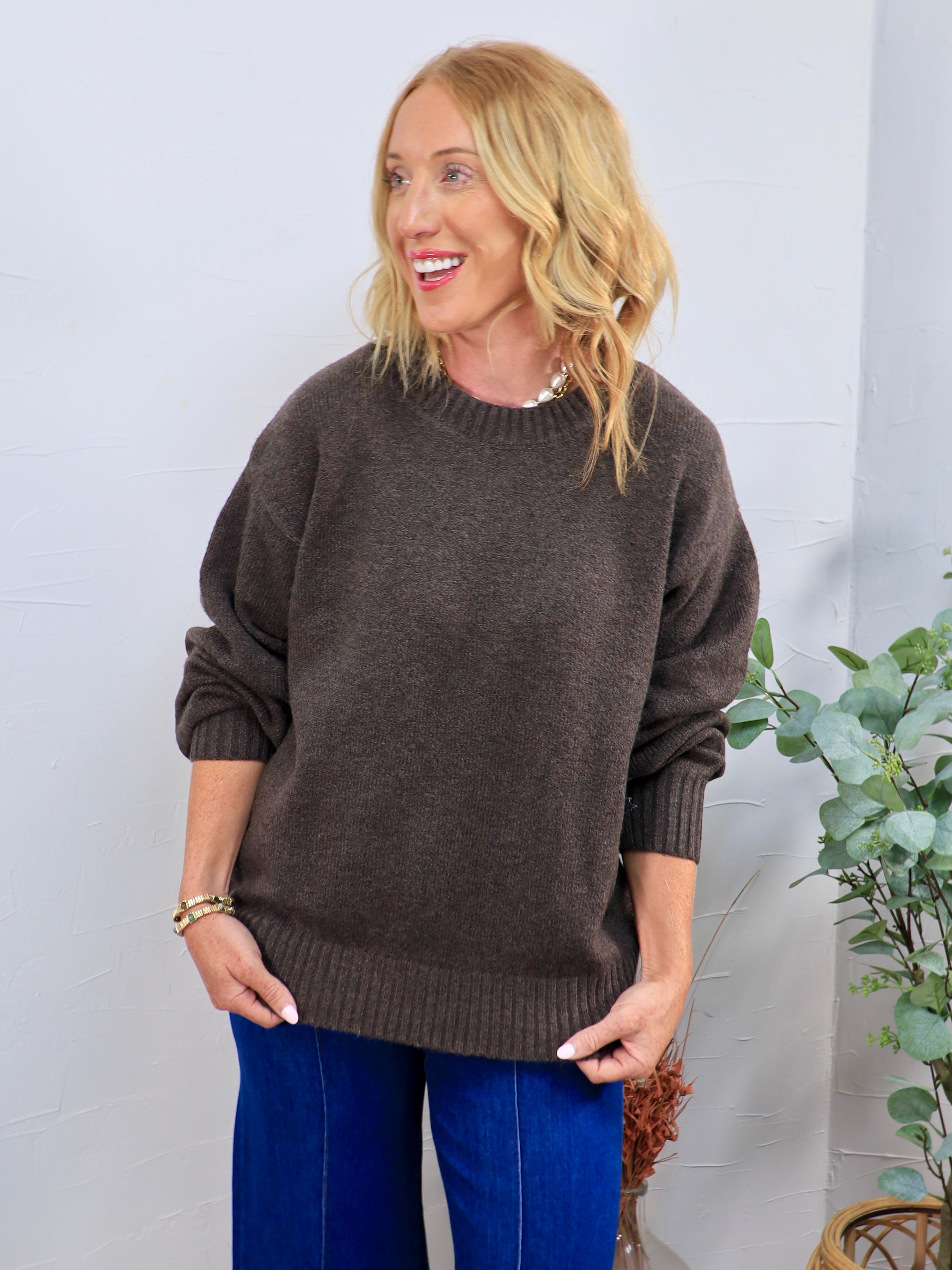 Chocolate brown oversized crewneck sweater styled with blue wide-leg jeans, featuring ribbed cuffs and hem.