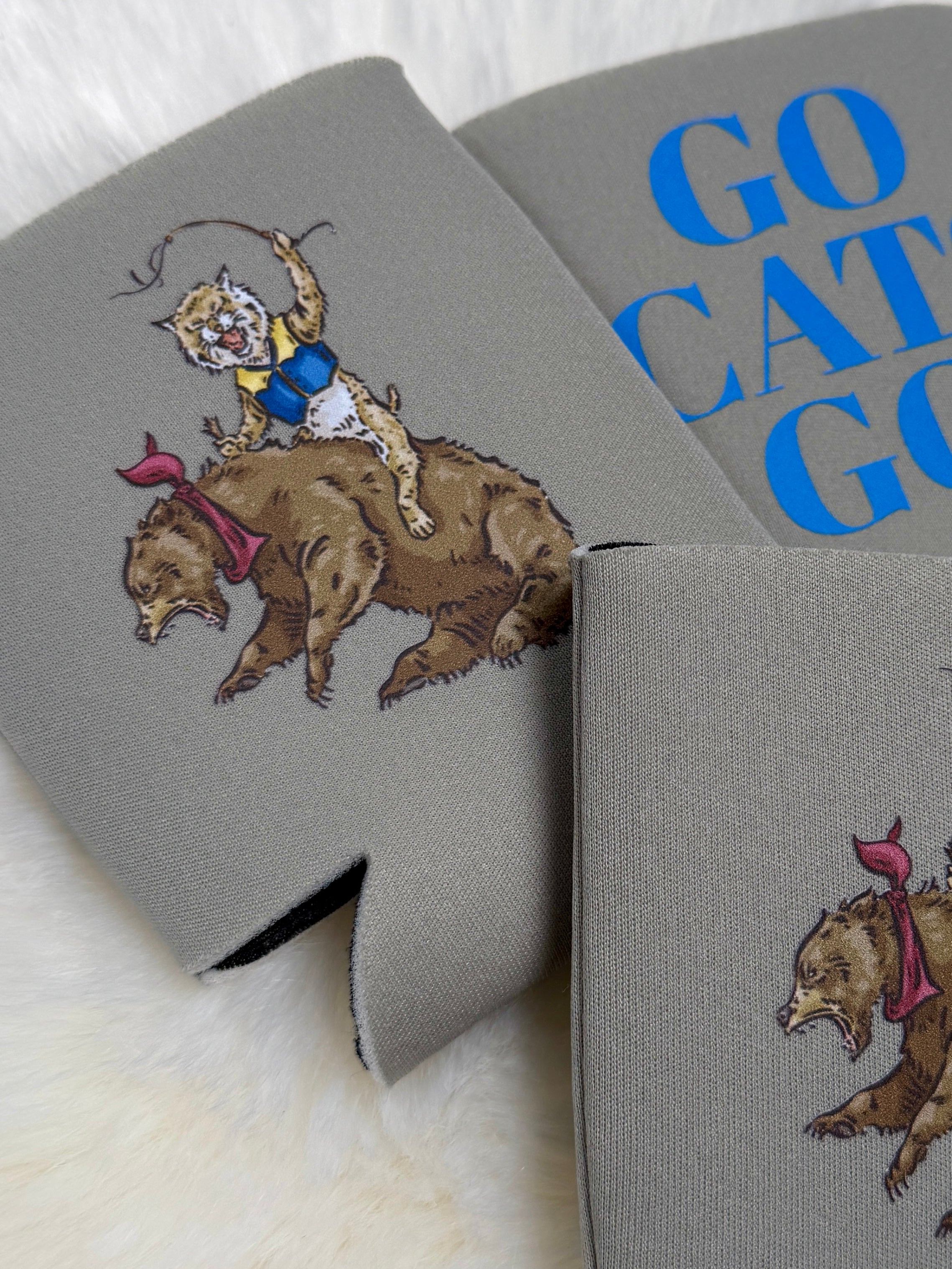 Gray neoprene koozie featuring illustrated wildcat riding a bear, with "Go Cats Go" text in blue.