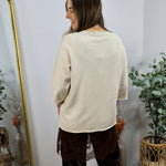 Cream short-sleeve knit sweater shown from behind, paired with dark brown velvet lace-trim trousers.