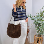Woman wearing navy striped polo sweater with white wide-leg jeans and brown studded shoulder bag