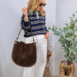 Woman wearing navy striped polo sweater with white wide-leg jeans and brown studded shoulder bag