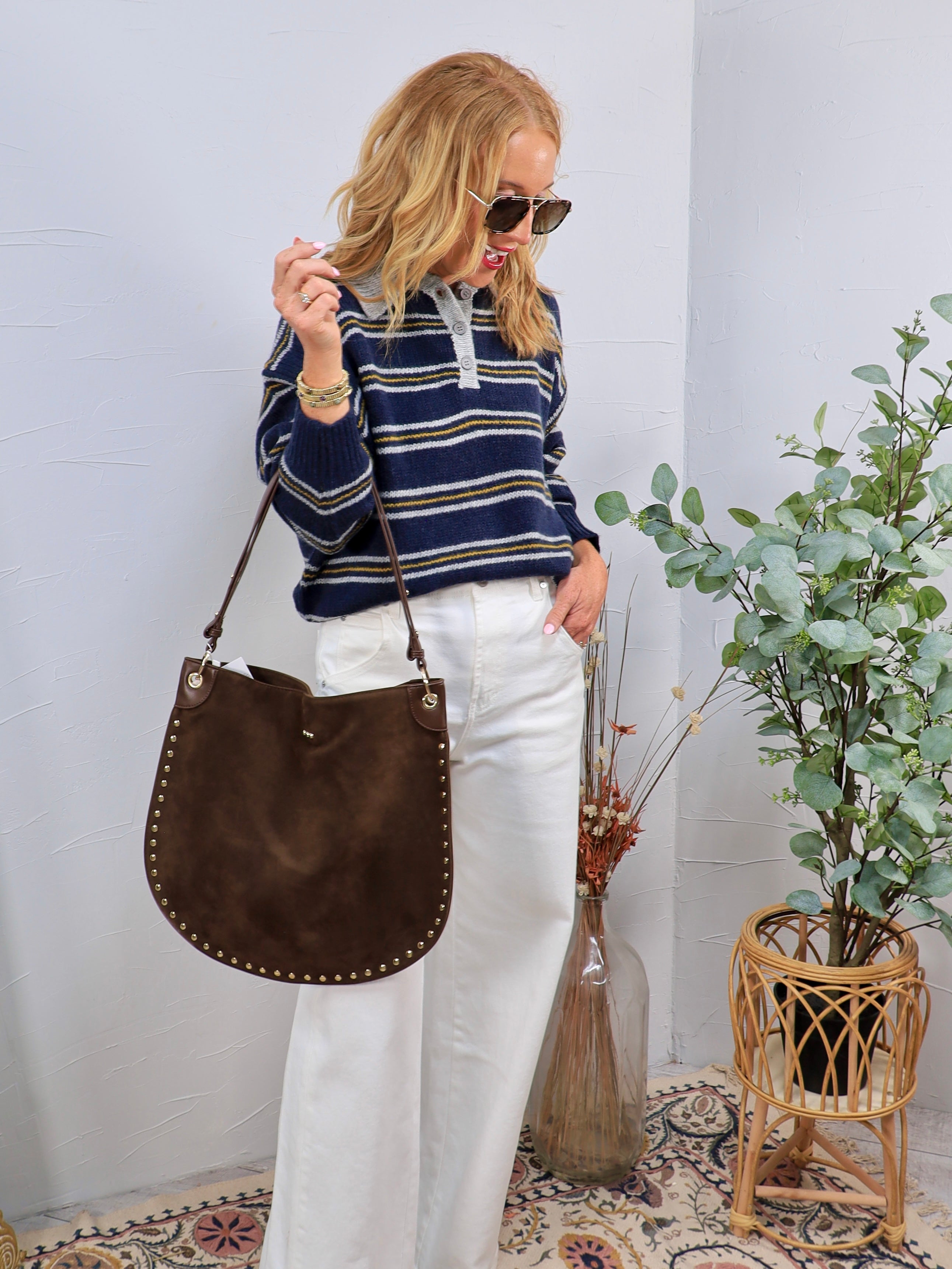 Woman wearing navy striped polo sweater with white wide-leg jeans and brown studded shoulder bag