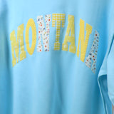 Light blue oversized mockneck sweater with yellow and floral patchwork Montana lettering across chest