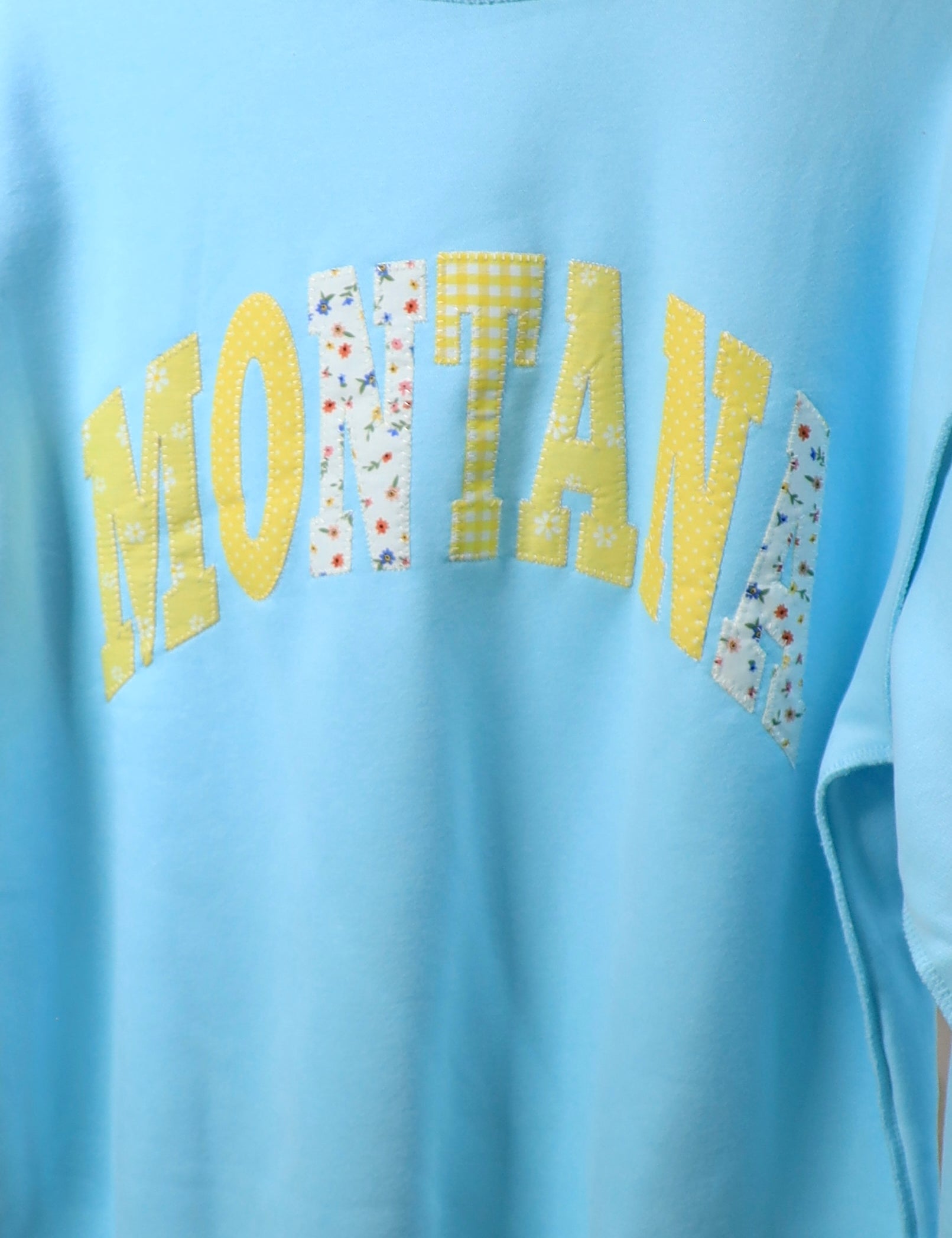 Light blue oversized mockneck sweater with yellow and floral patchwork Montana lettering across chest