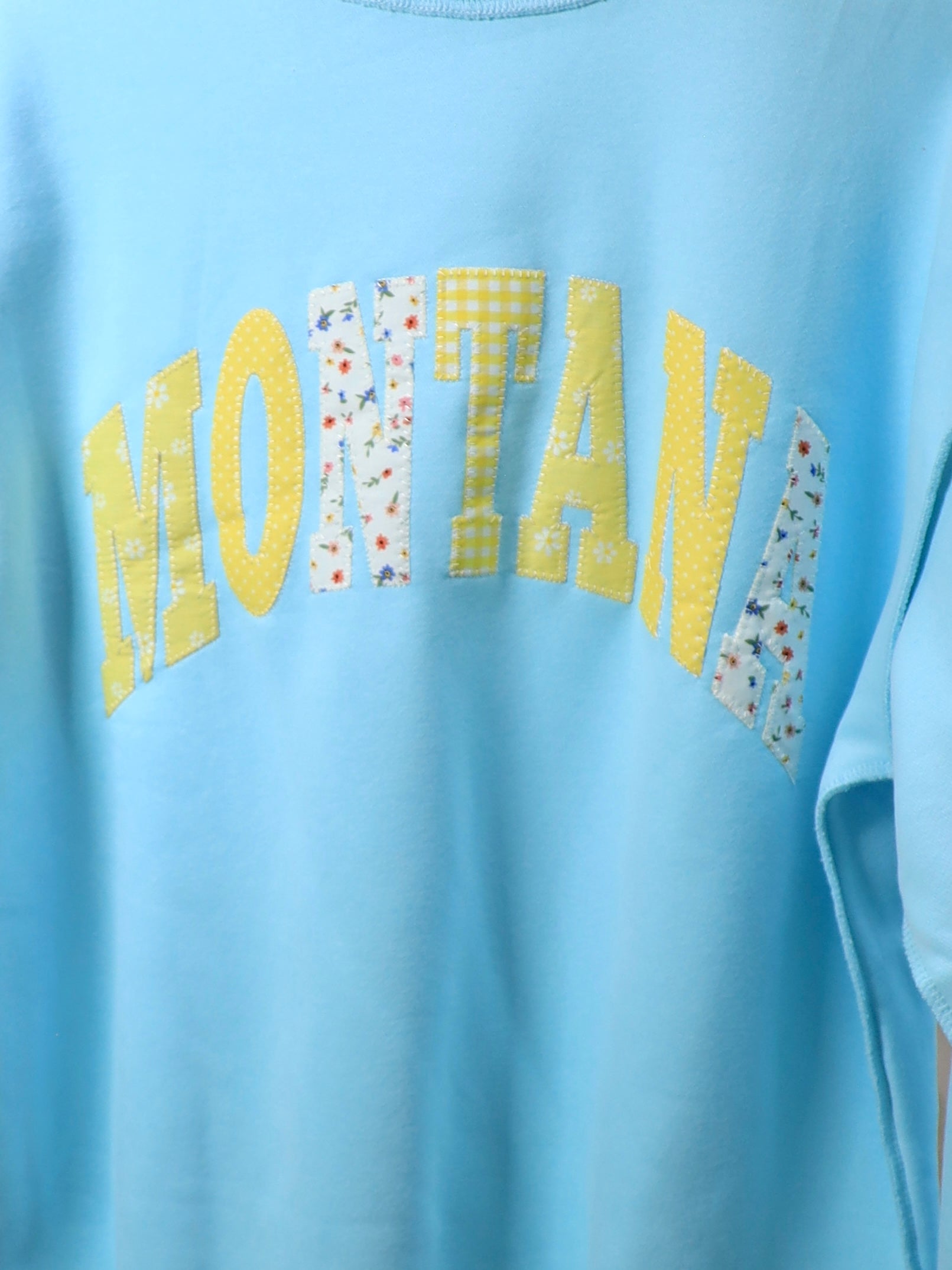 Light blue oversized mockneck sweater with yellow and floral patchwork Montana lettering across chest