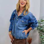 Oversized medium-wash denim jacket with silver buttons, chest pockets, worn over a brown mini skirt.