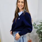 Woman wearing navy blue contrast collar pullover sweater layered over a striped blue collared shirt with light-wash jeans