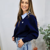 Woman wearing navy blue contrast collar pullover sweater layered over a striped blue collared shirt with light-wash jeans