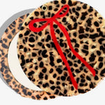 Round compact mirror with leopard print tortoiseshell design and decorative red ribbon bow accent.