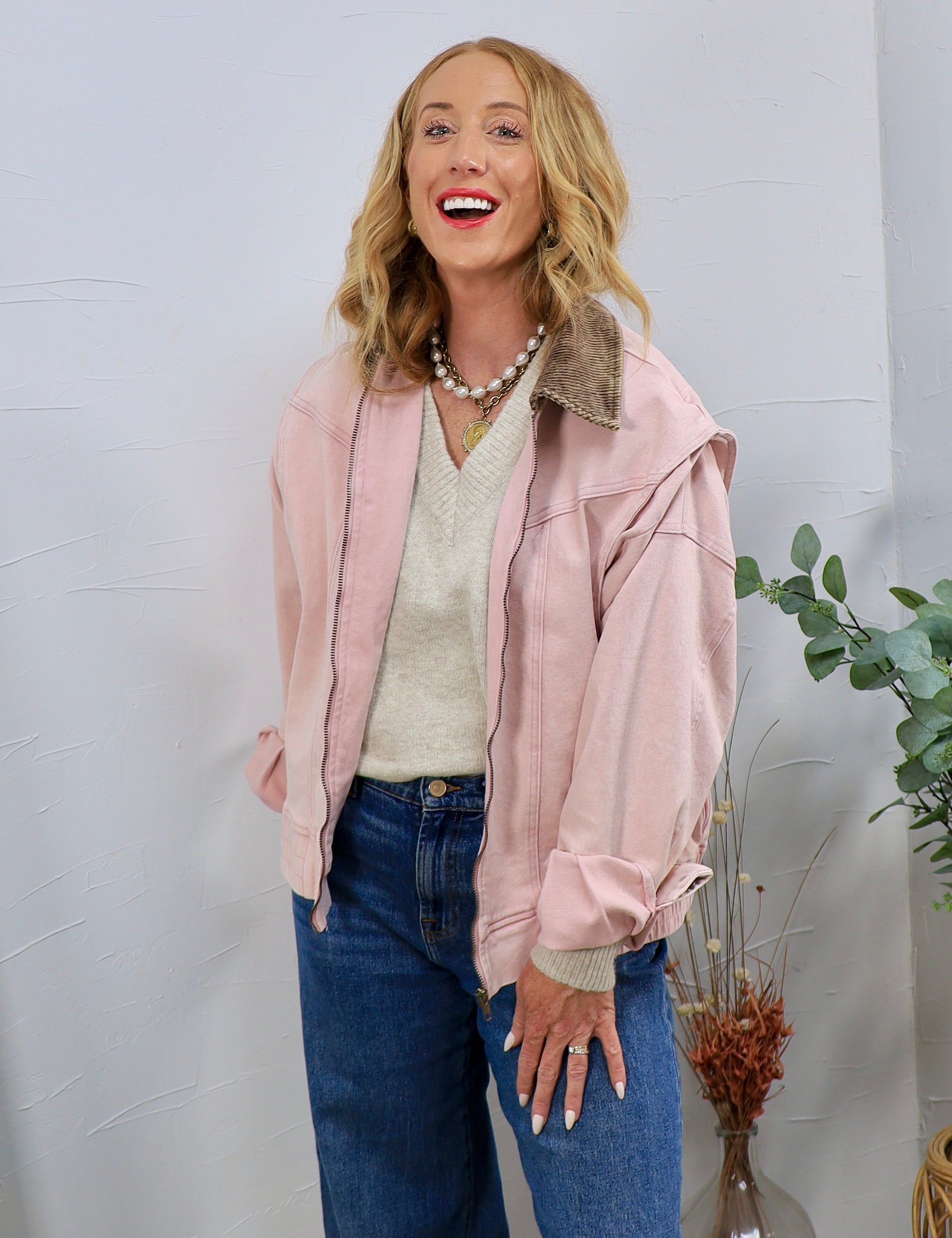 Dusty rose zip-up bomber jacket with corduroy collar, styled over cream V-neck sweater and blue jeans.