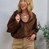 Woman wearing a cropped chocolate brown hooded bomber jacket with khaki wide-leg pants and gold necklace