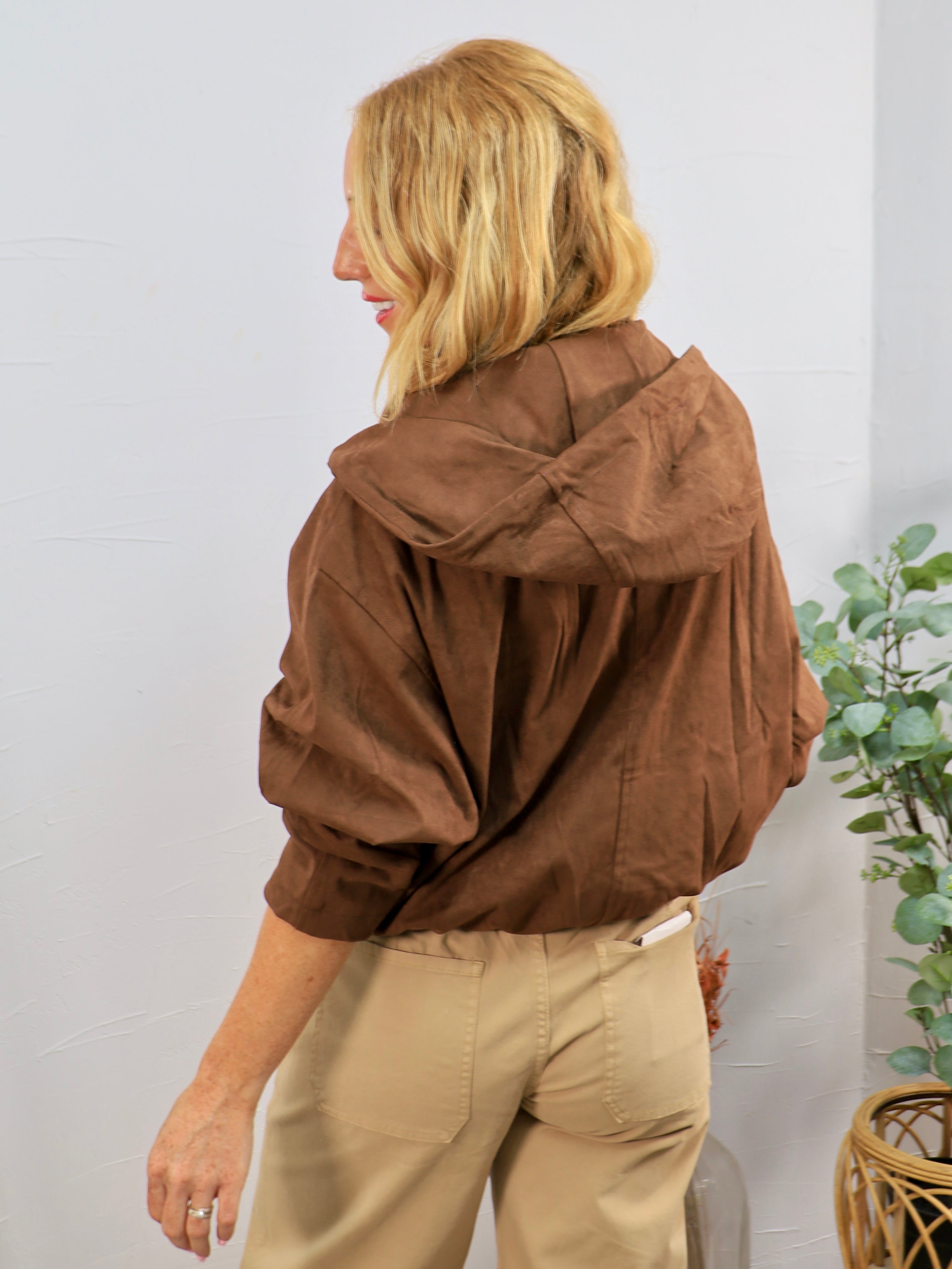 Brown hooded bomber jacket with voluminous sleeves, styled with khaki pants, shown from back angle.