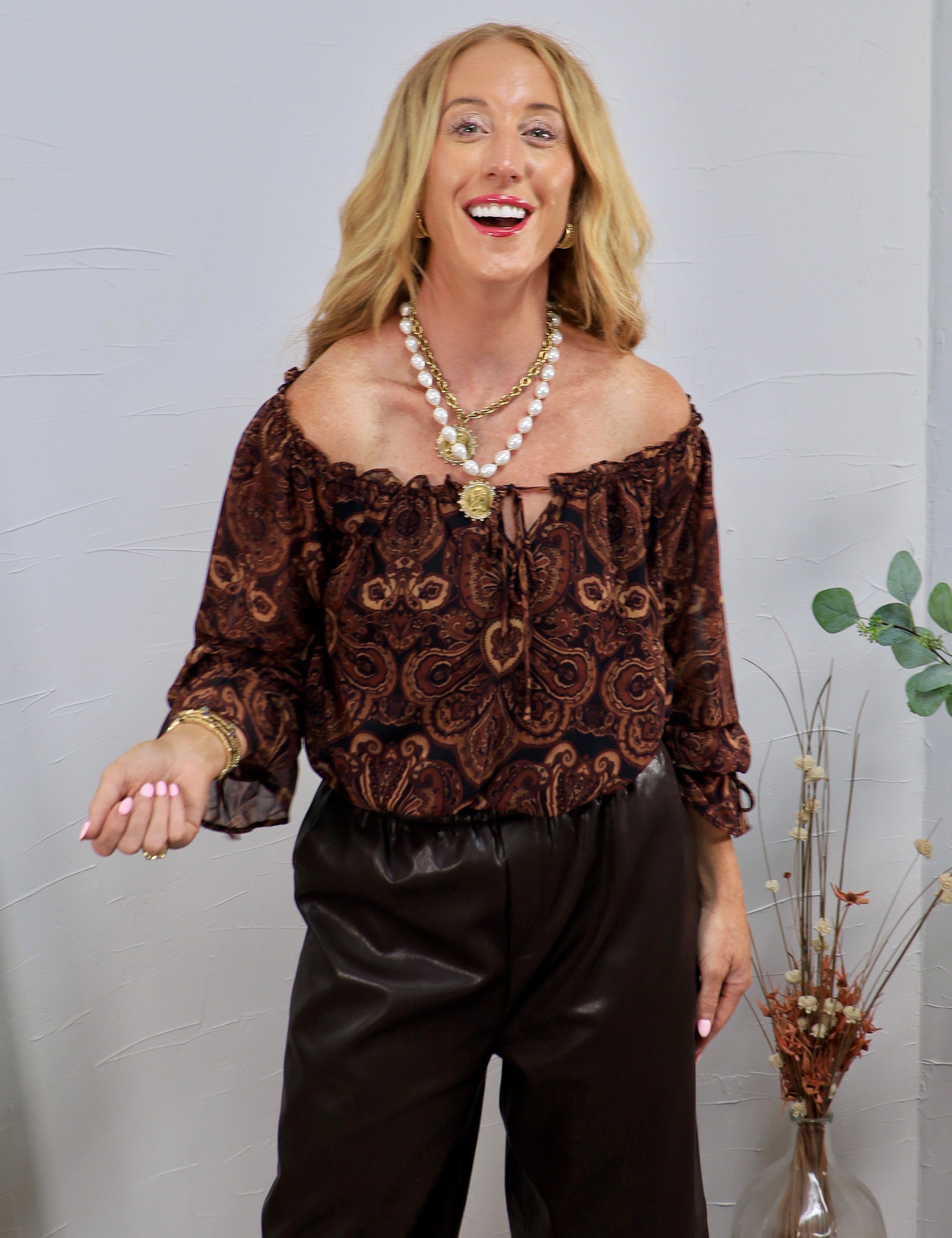 Brown and black paisley off-shoulder blouse with ruffle neckline, tie detail, and three-quarter sleeves.