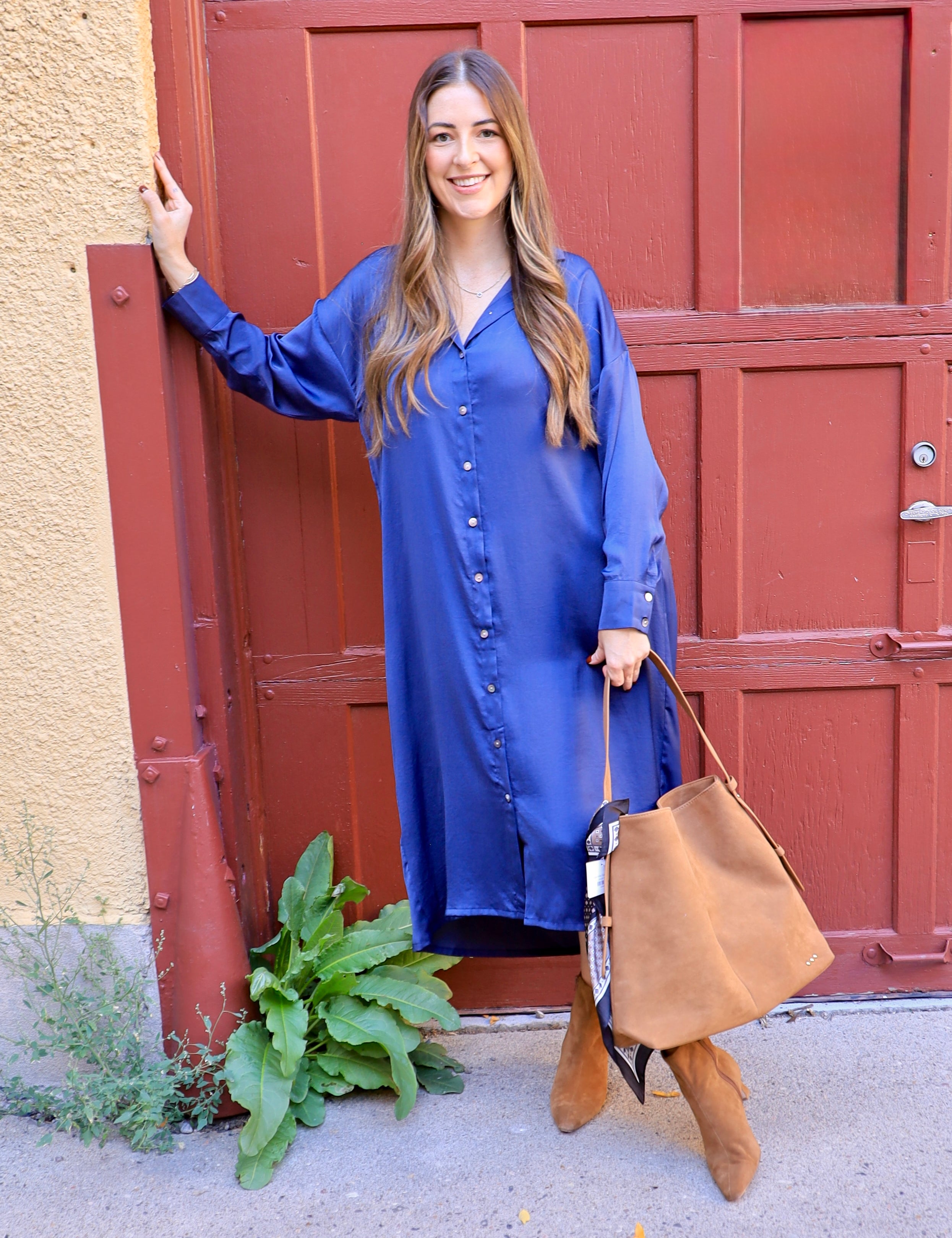 Woman in cobalt blue satin button-front maxi dress with tan suede boots and tote bag